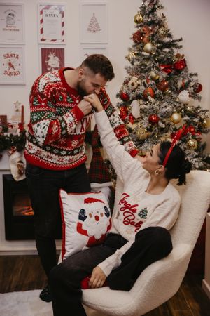 Playful Christmas portrait with couple in festive sweaters sharing intimate moment by decorated tree.
