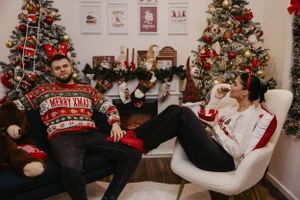 Cozy holiday scene with two people relaxing in chairs by Christmas tree and fireplace.