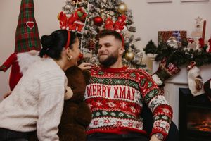 Intimate holiday moment captured between couple in Christmas sweaters by decorated tree.