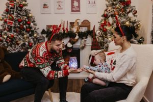 Holiday family moment with baby and adults by Christmas tree and decorative wall art.