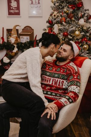 Couple sharing an intimate holiday moment in front of a decorated Christmas tree in a cozy living room setting.