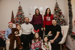 A group poses together in a festive holiday setting with decorated Christmas trees and holiday decor in the background.