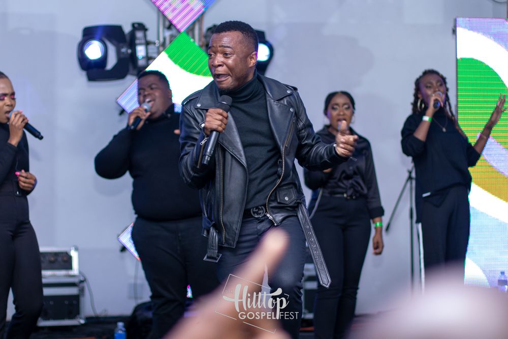 Dynamic performer in black leather jacket singing on stage with backup singers.
