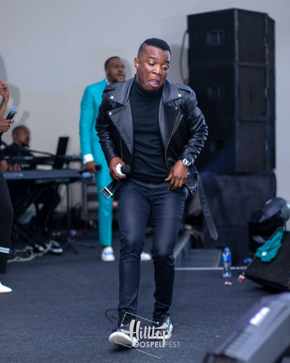 A performer in a black leather jacket and dark outfit dances during a stage performance.