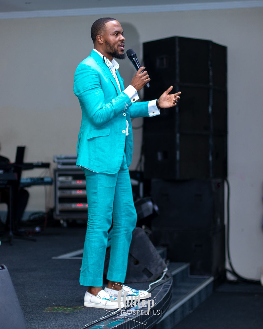 A performer wearing a vibrant turquoise suit speaks into a microphone on stage.