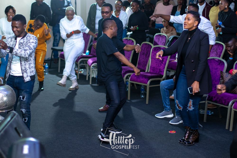 People dancing and socializing at an event with distinctive purple chairs in the background.