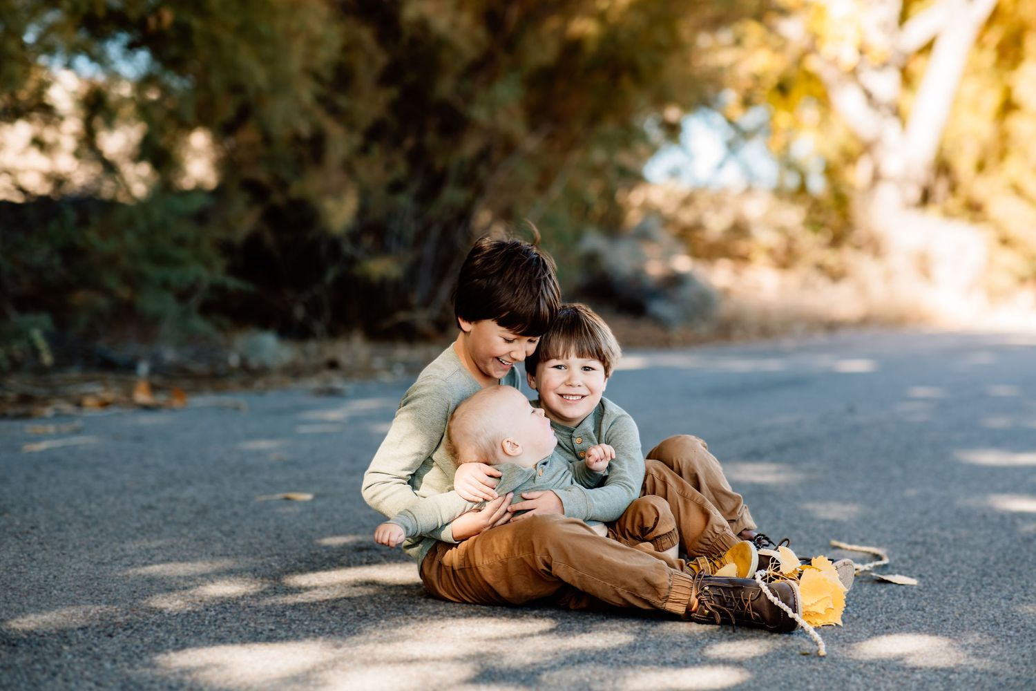 A tender parental moment captured on a sunlit path with warm autumn tones and natural lighting.