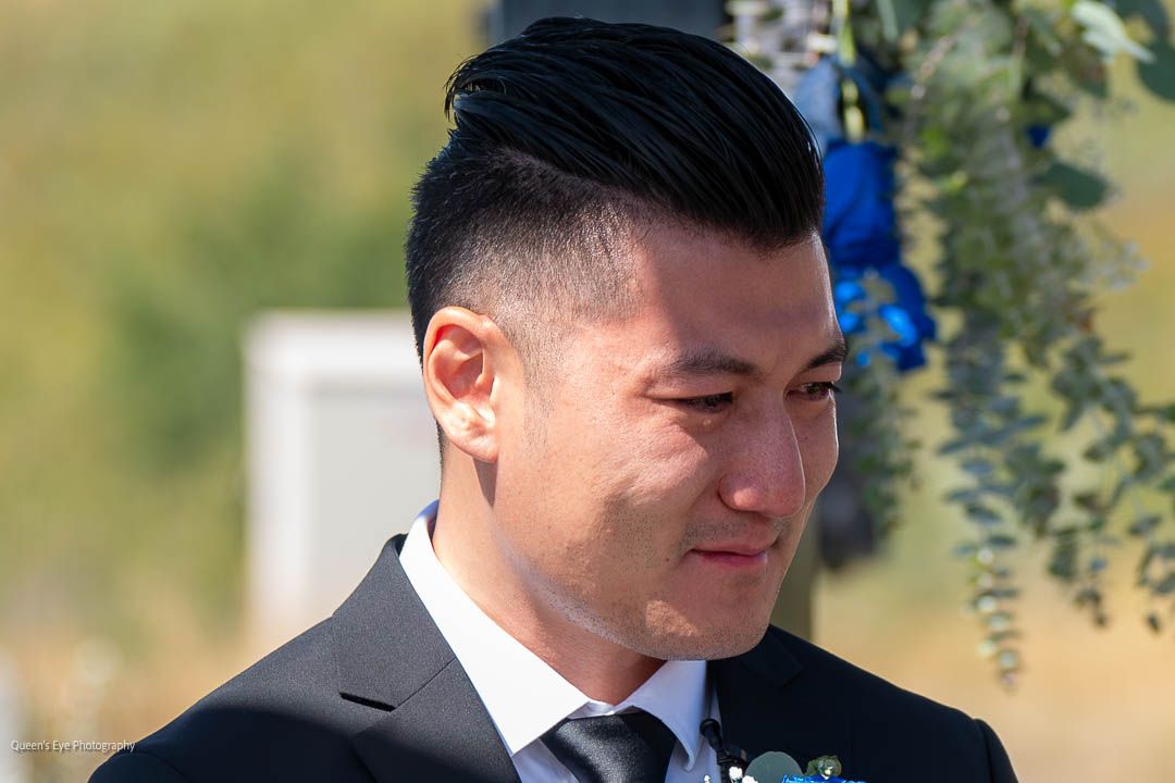 An Asian man waiting at the alter as tears fall down his face.