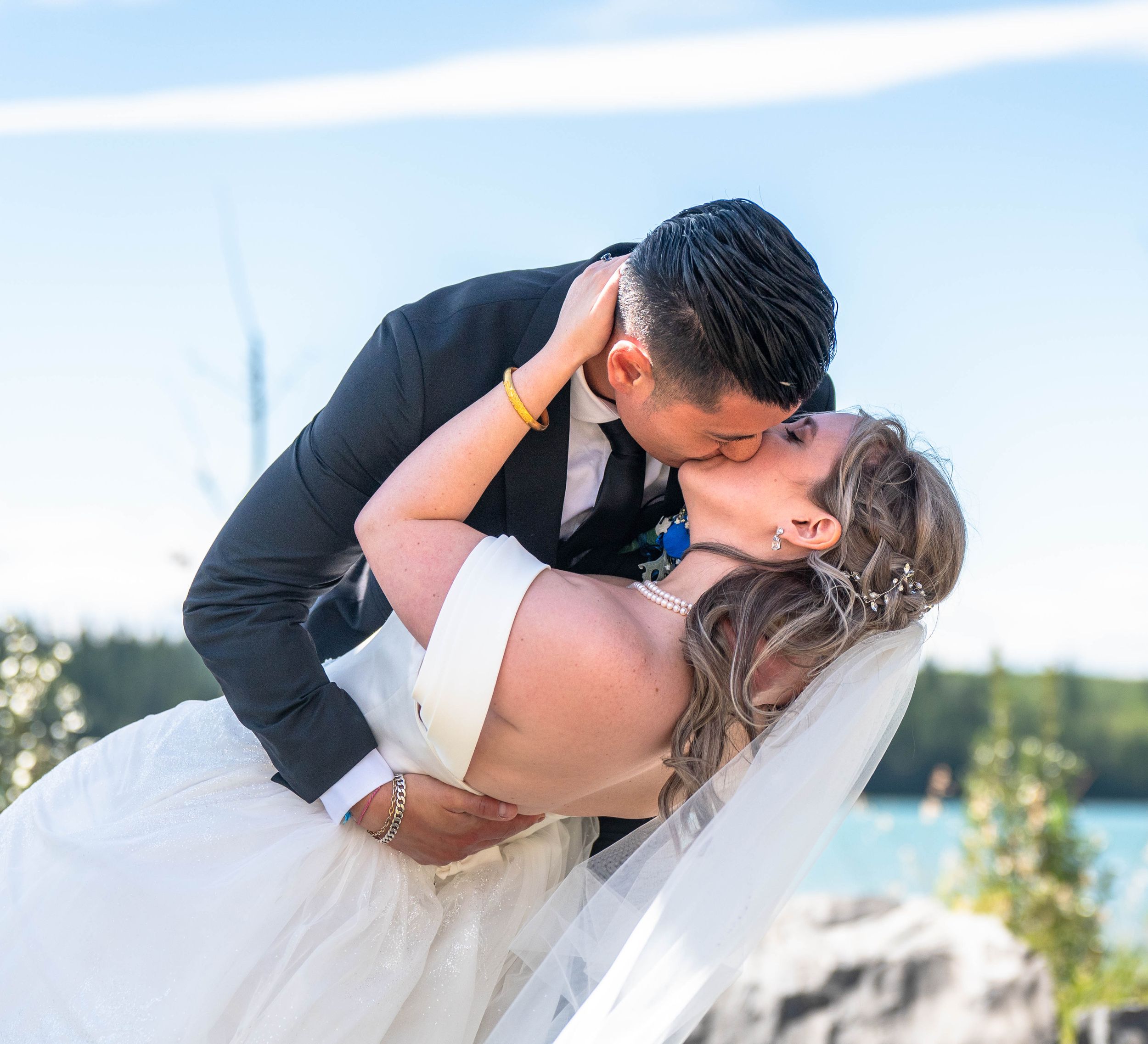 A man kisses his wife for the first time as he dips her. The beautiful blue skys and lake frame the kiss.