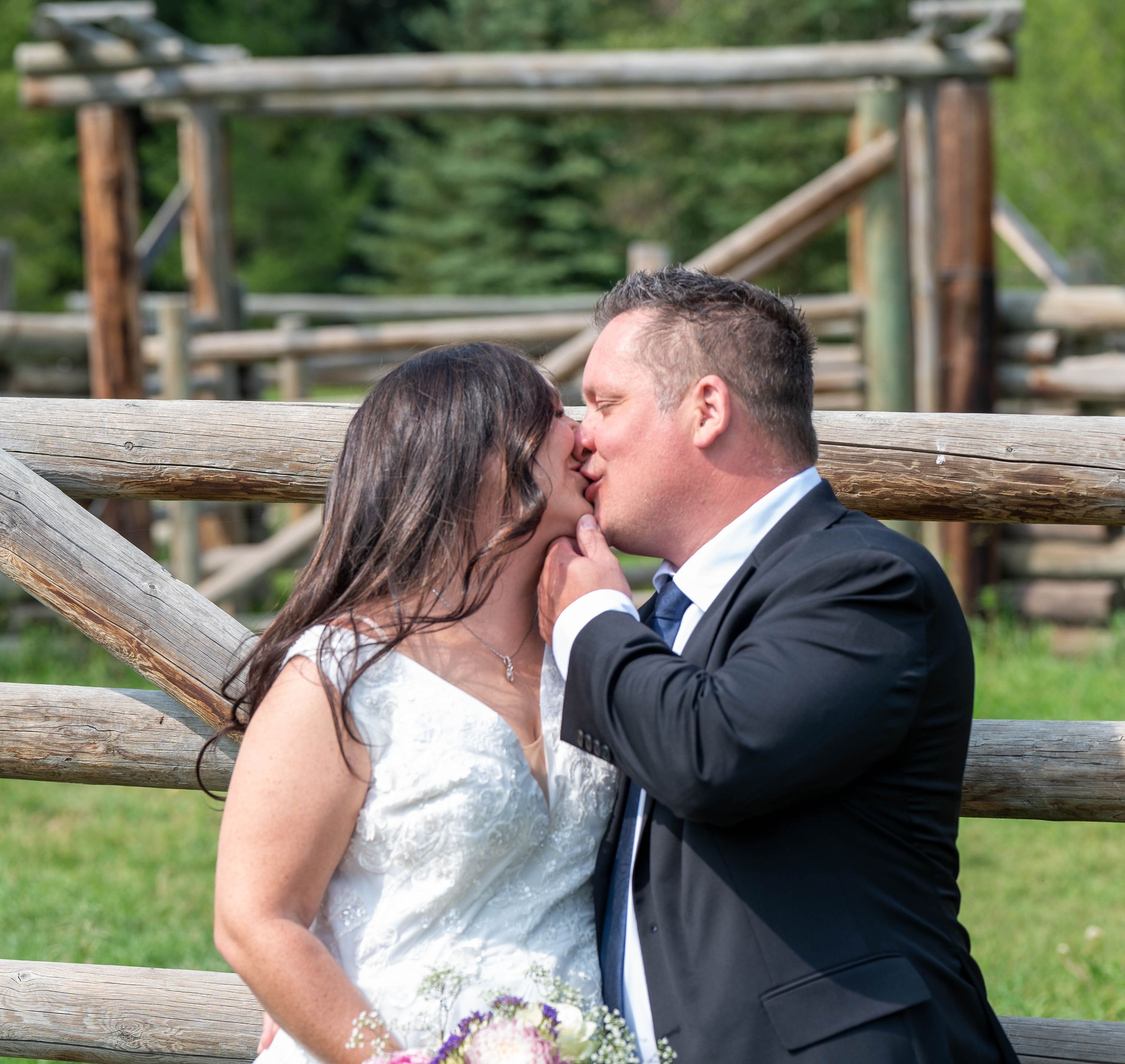 A man kisses his wife with a beautiful corral behind them. His hand on her chin so that he can have his fill of her lips,.