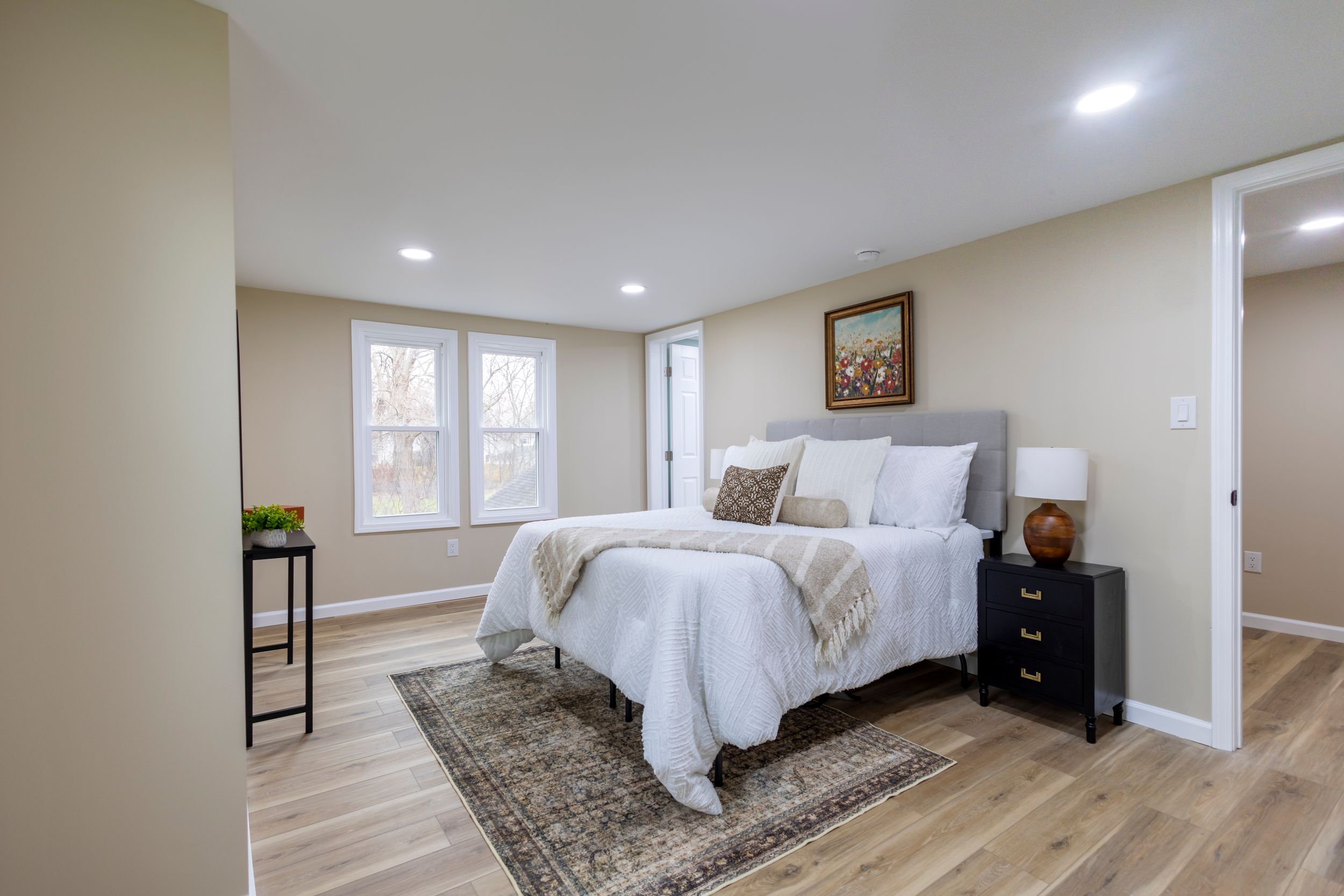 Modern bedroom interior with white bedding, recessed lighting, and hardwood floors in a contemporary home setting.