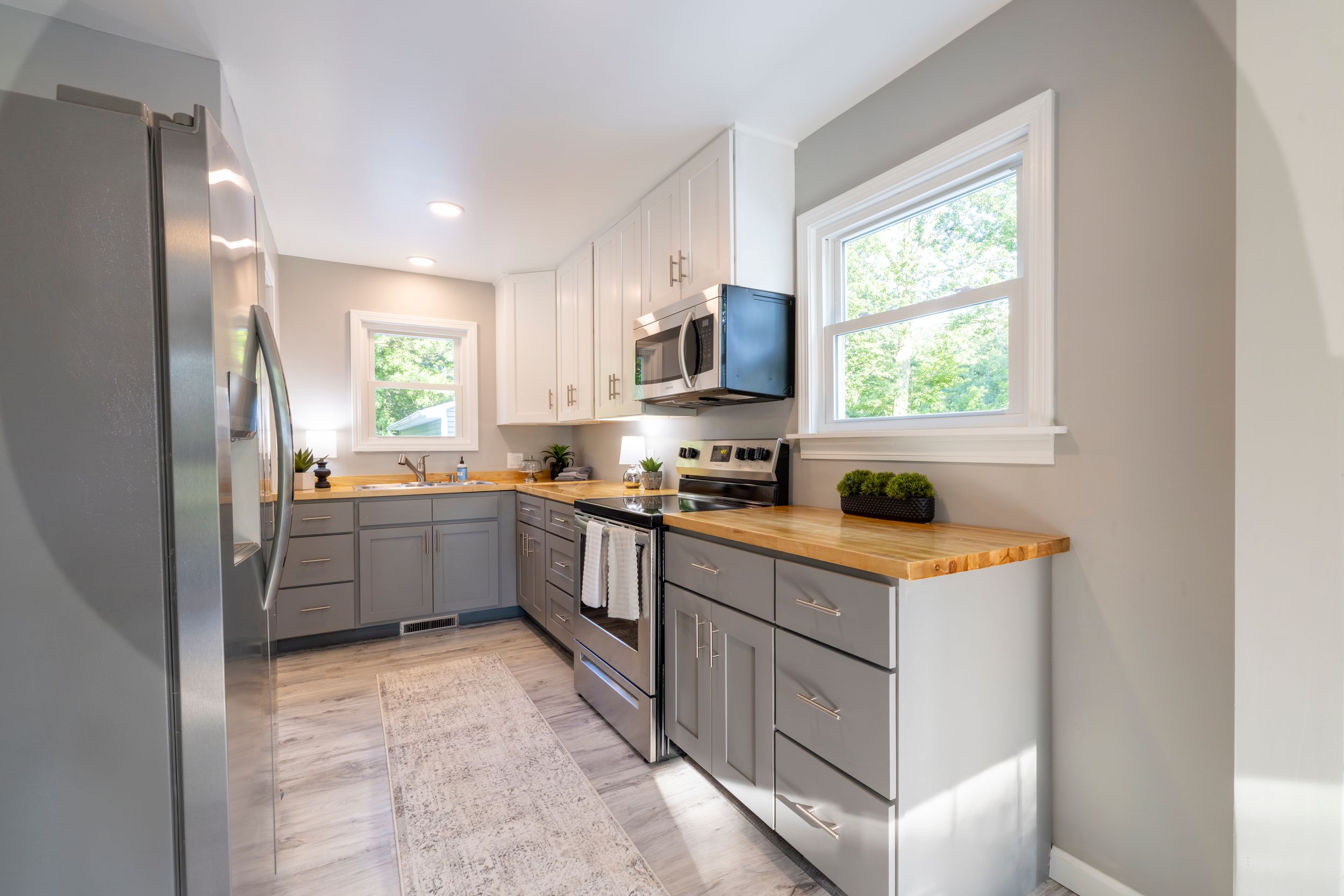 Modern kitchen with grey cabinets, butcher block countertops, stainless appliances and natural light from window.