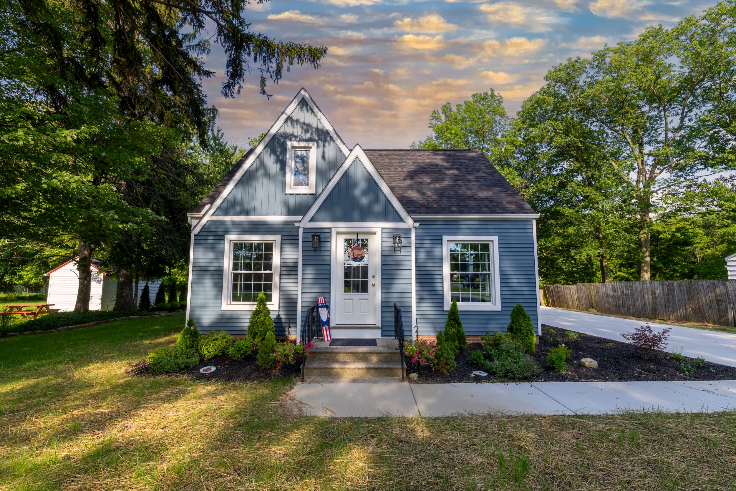 A charming blue cottage-style house with white trim and dormer windows glows in the warm light of sunset.