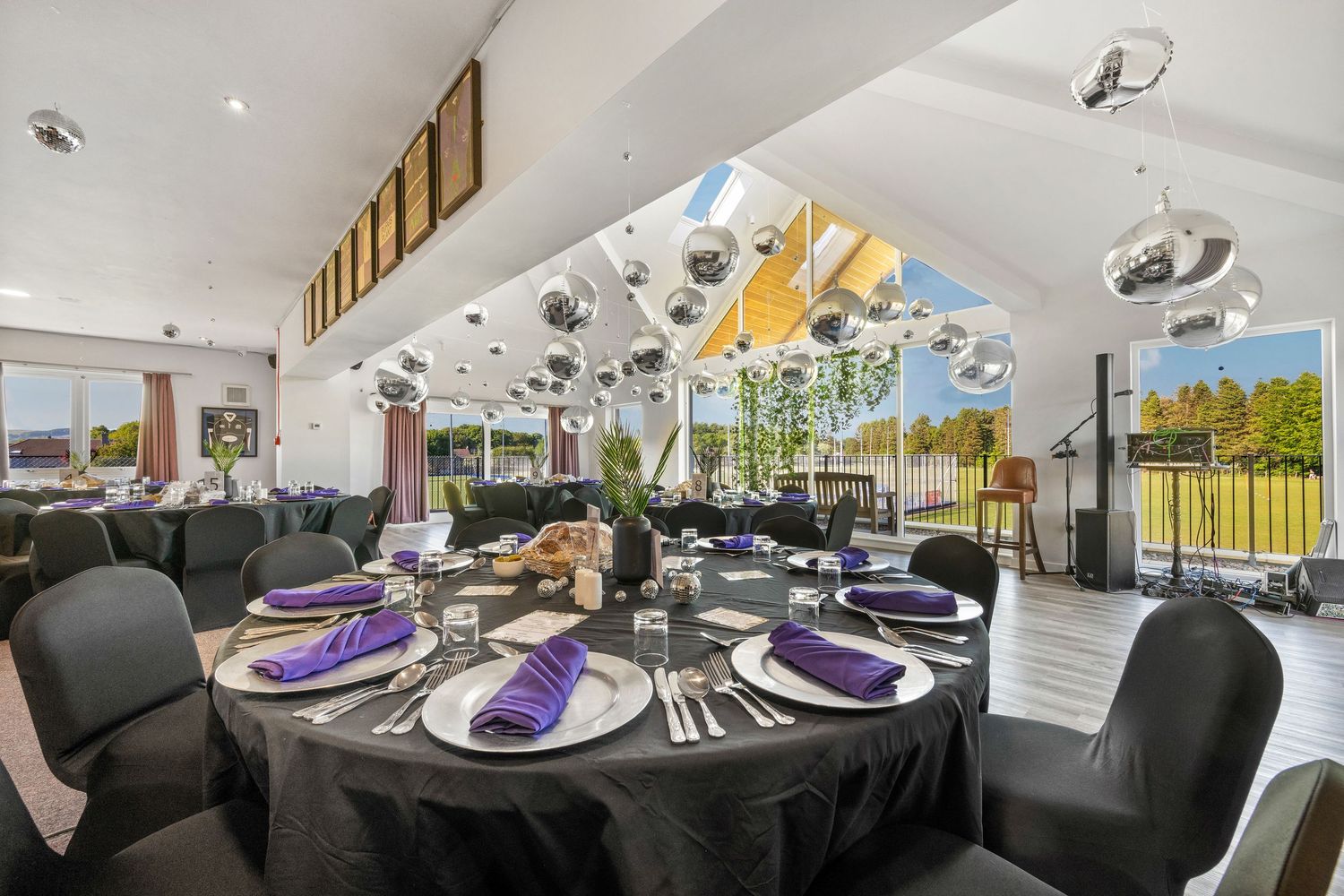 Elegant dining table settings with black tablecloths and purple accents in a bright modern space.