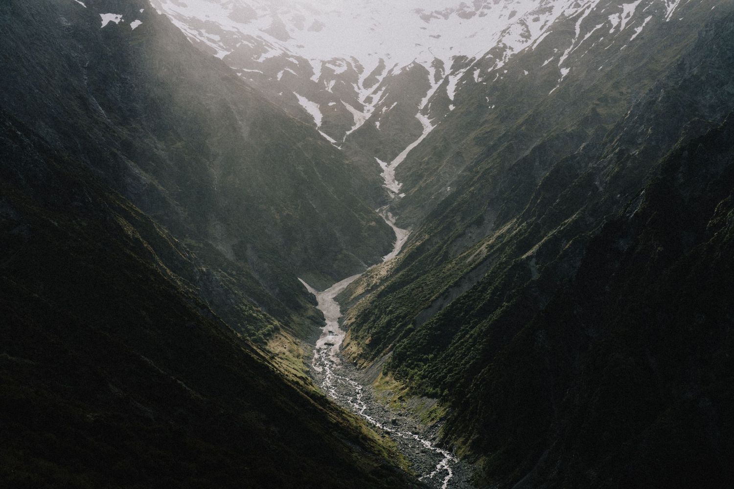 Aerial view of a deep valley with a winding river and snow-capped peaks in New Zealand.