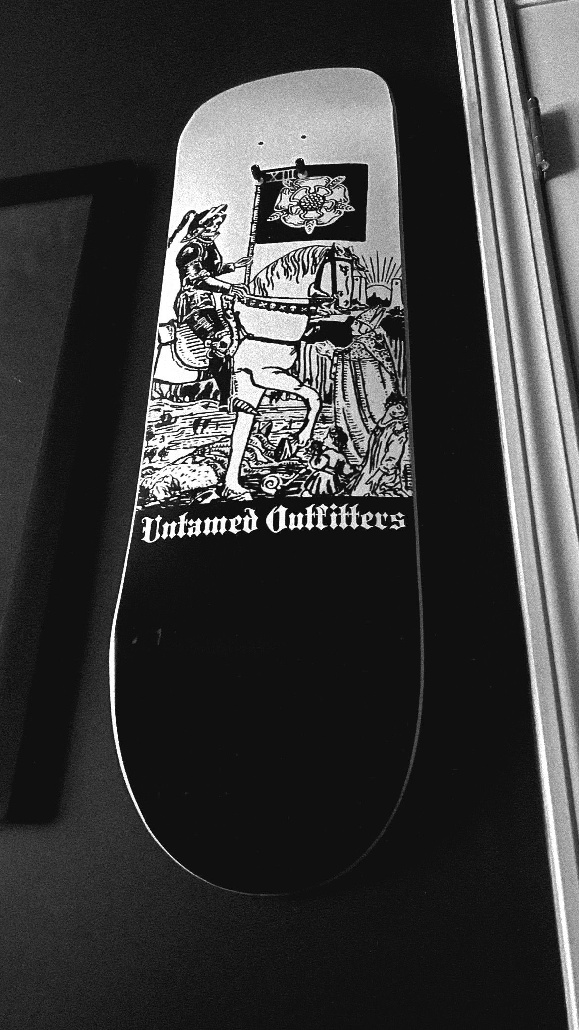 Black and white skateboard deck featuring Untamed Outfitters brand with medieval knight on horseback graphic art.