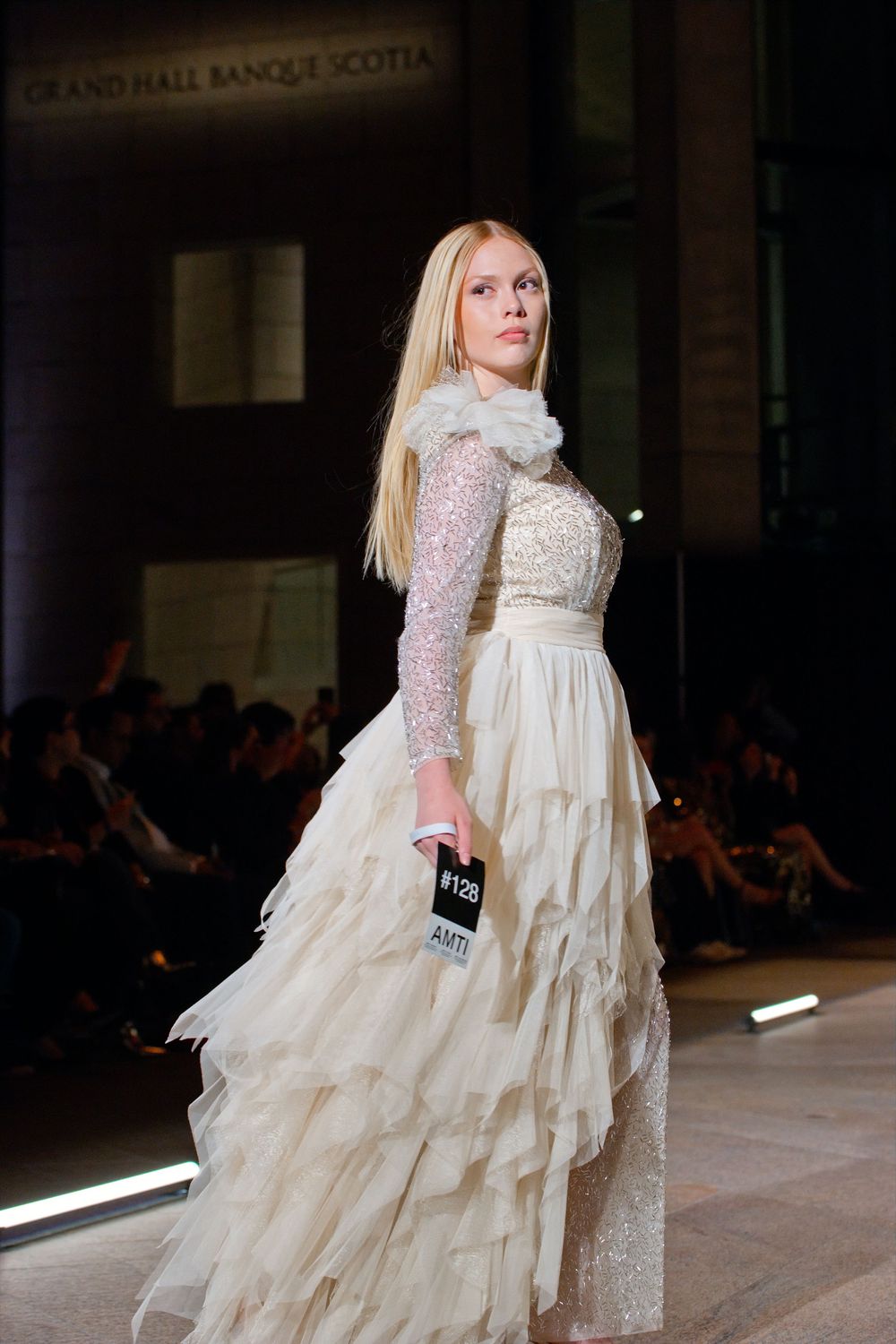 Model showcases elegant ivory ruffled gown with lace bodice at Grand Hall Banque Scotia fashion event.