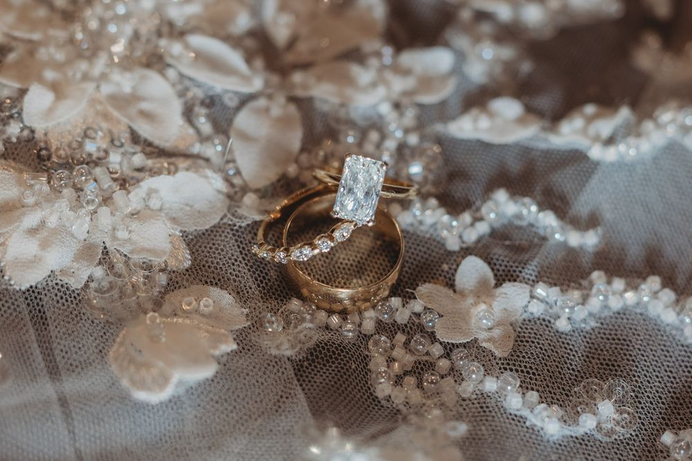 Gold wedding band and diamond engagement ring resting on delicate floral lace bridal veil.