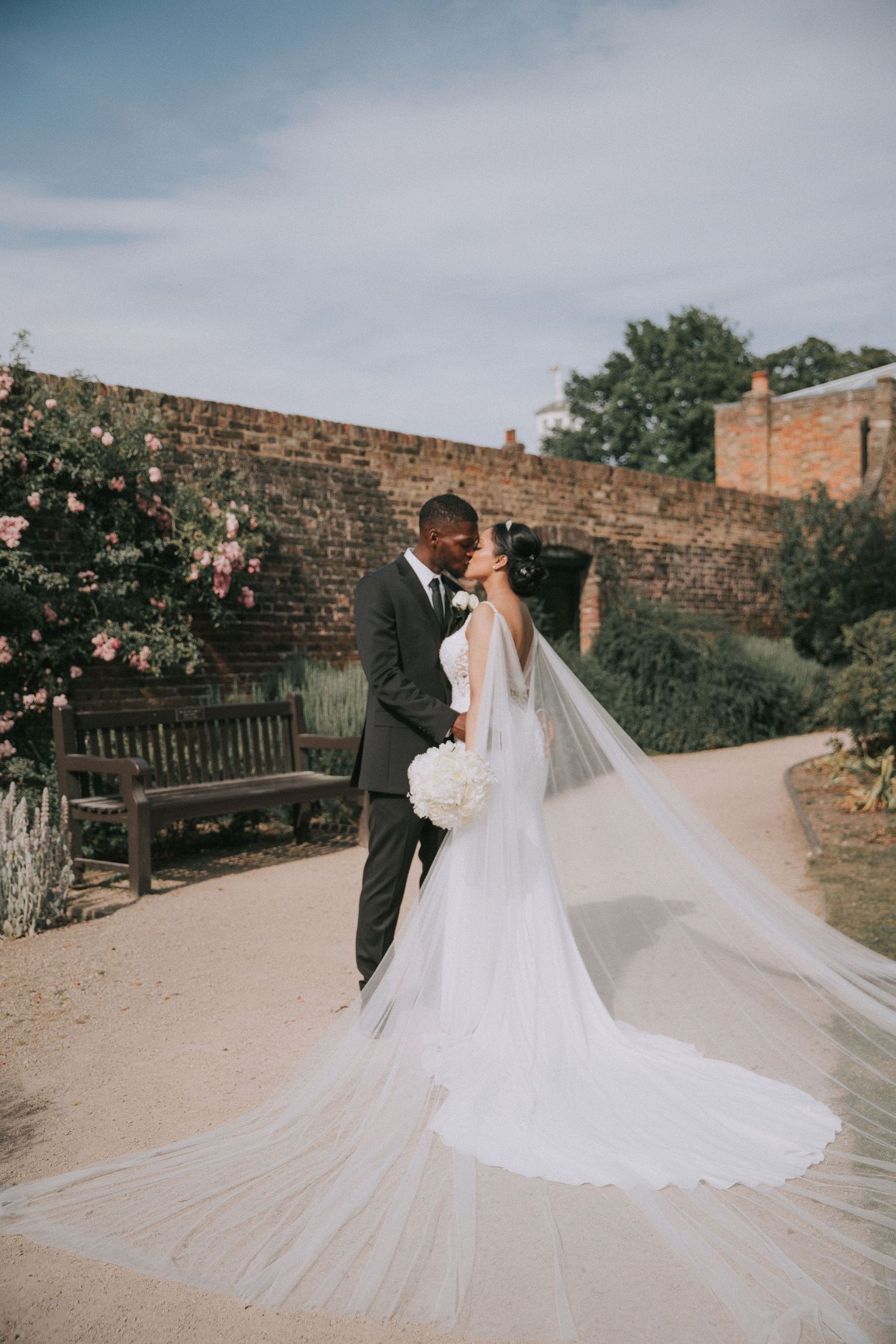 Bride and groom descend stone steps of elegant classical building, bride holding white bouquet in sunlight.