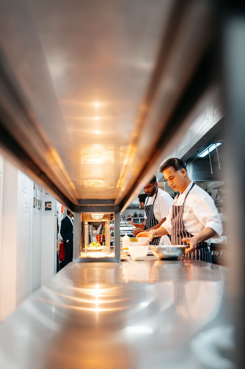 Chefs in aprons preparing dishes in a modern professional restaurant kitchen with stainless steel counters.