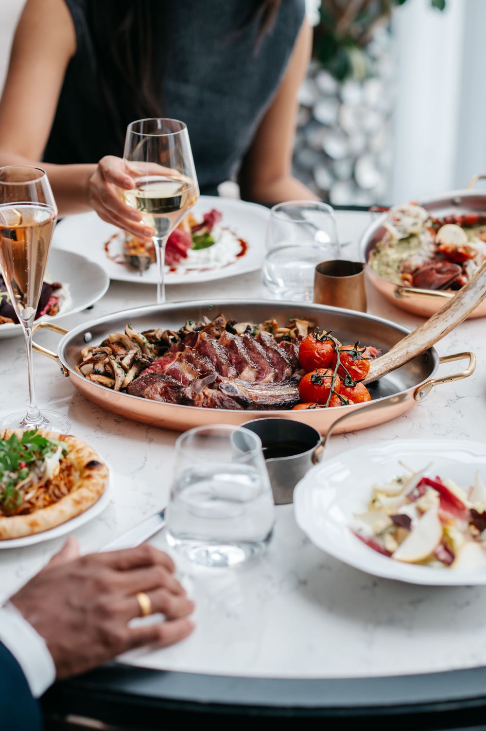 Elegant restaurant table with grilled steak, roasted tomatoes, and wine glasses shared by diners.