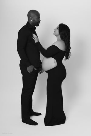 Black and white maternity photo of a pregnant woman in a black gown posing with a man in all black attire family portrait session in PA