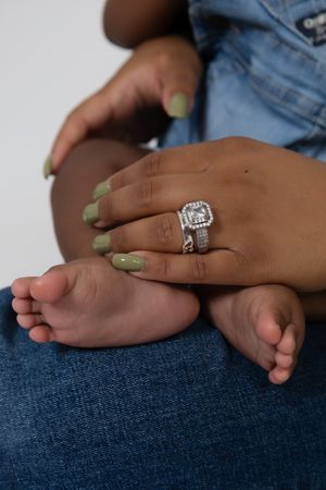 A mother's hand with green nails and a diamond ring rests on her baby's tiny feet, wearing jeans family portrait session in Pittsburgh