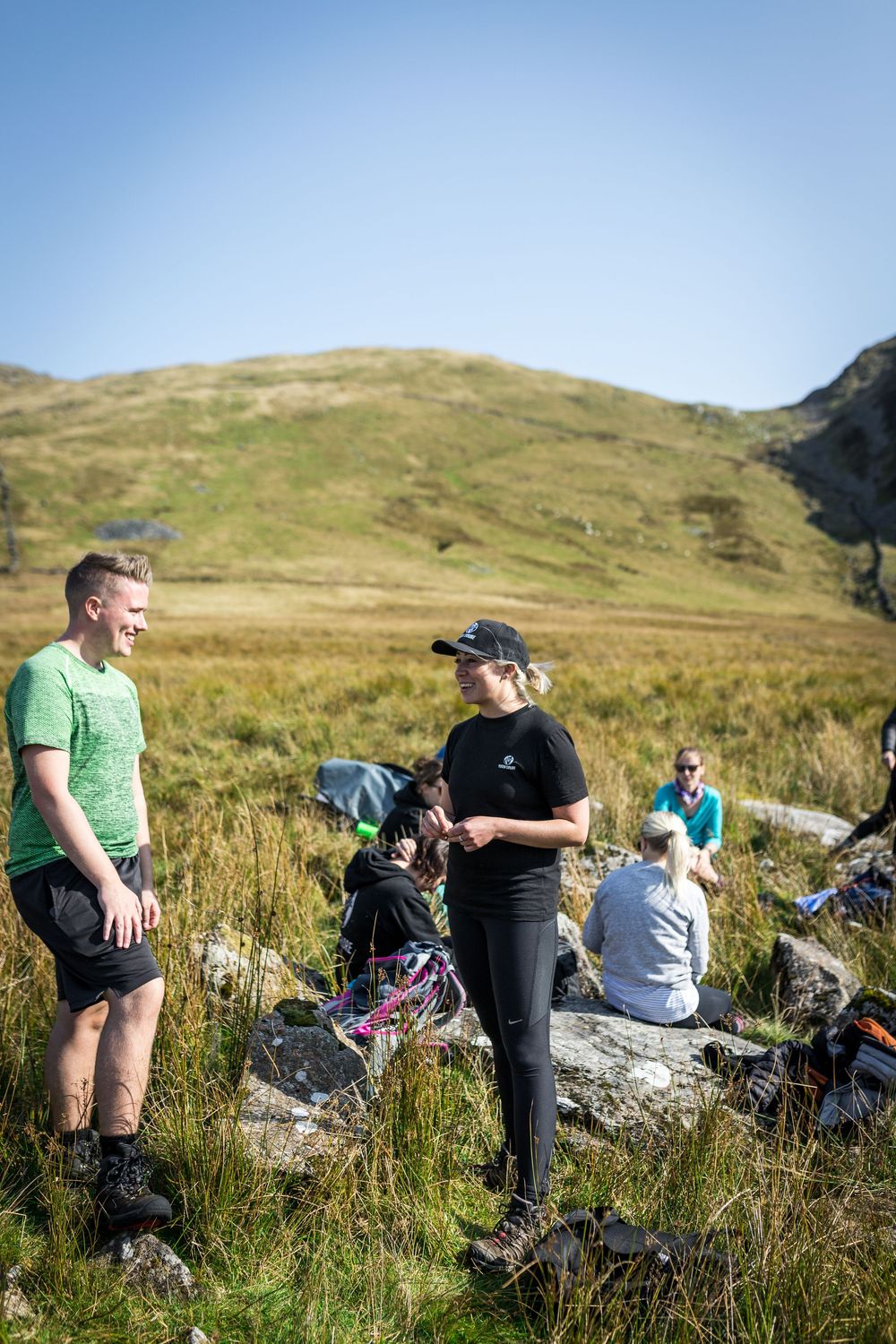 Hikers resting on rocks in a scenic highland landscape under a clear blue sky on a sunny day.