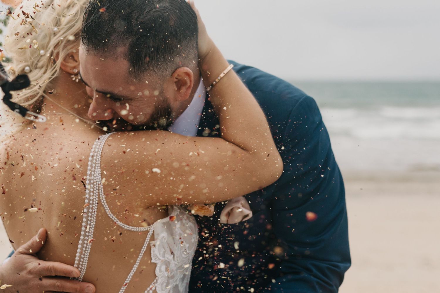 Bride and groom embracing on beach with confetti falling during romantic outdoor wedding ceremony. Coronado Island elopement