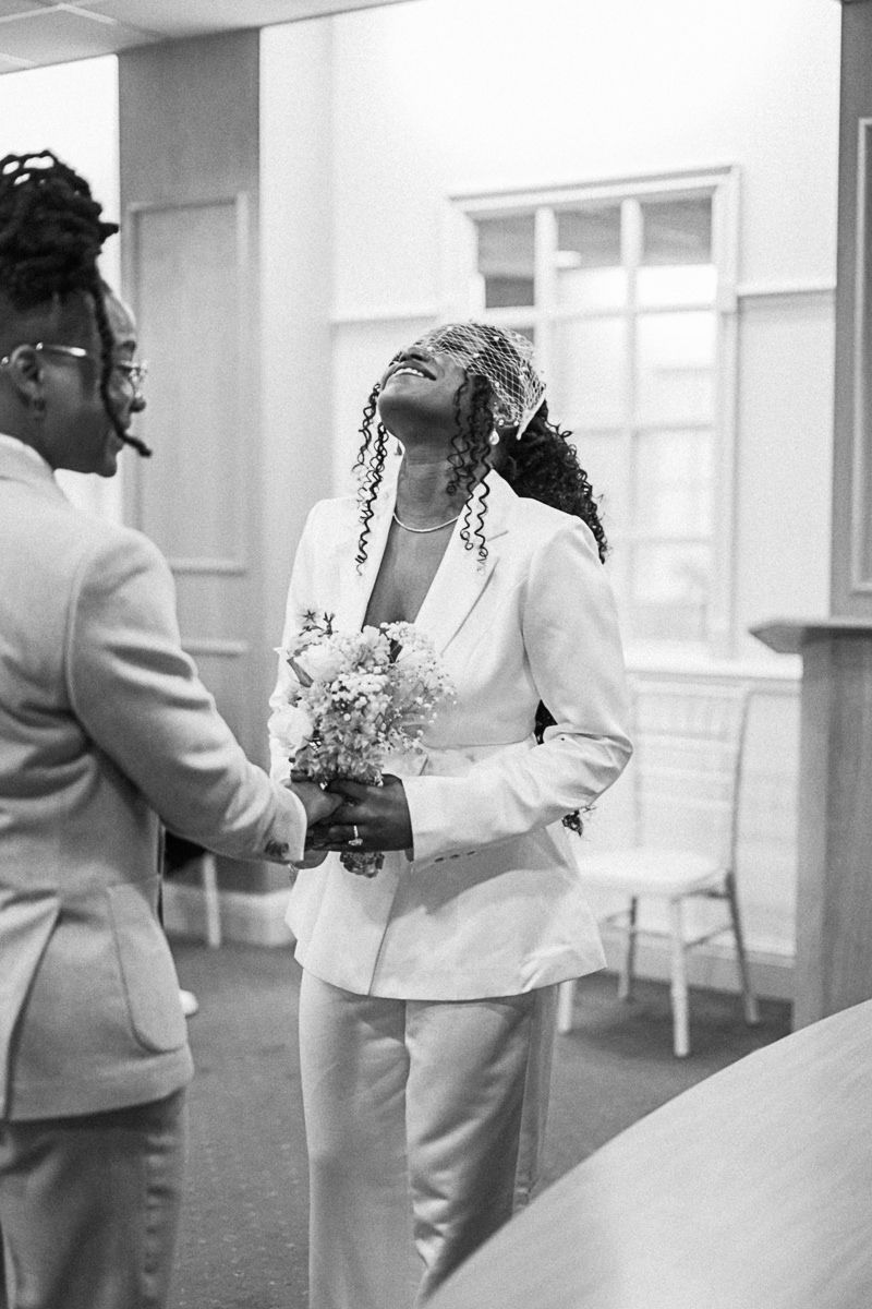 Black and white photo of two people in white suits holding flowers at a wedding ceremony.