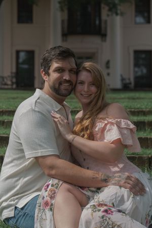 Smiling couple embracing on outdoor steps with a white columned mansion in the background.