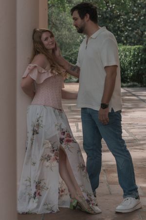 Couple sharing an intimate moment under a shaded portico, woman in a floral maxi dress.