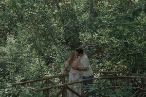 Couple sharing a tender kiss on a rustic wooden bridge surrounded by dense green forest.
