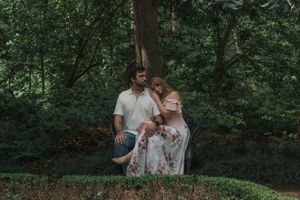 Couple sitting together among lush green bushes and trees in a romantic outdoor garden setting.