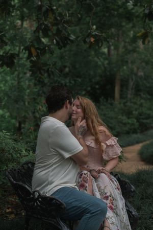 Romantic couple sharing an intimate moment on a bench surrounded by green trees in a garden.