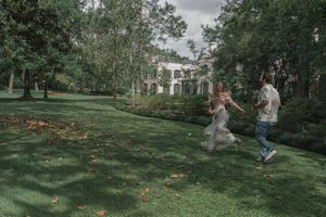 Couple running and playing together on a green lawn with a historic mansion in the background.