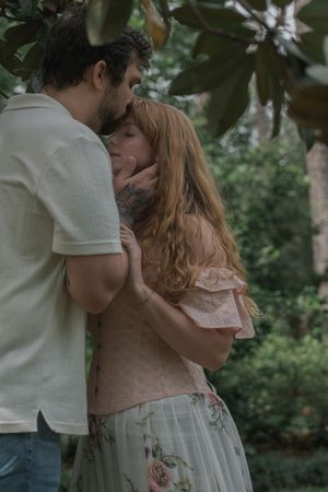 Couple sharing a tender embrace under magnolia tree branches in a lush green garden setting.