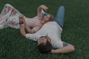 Couple lying on green grass together, sharing a relaxed and romantic outdoor moment.