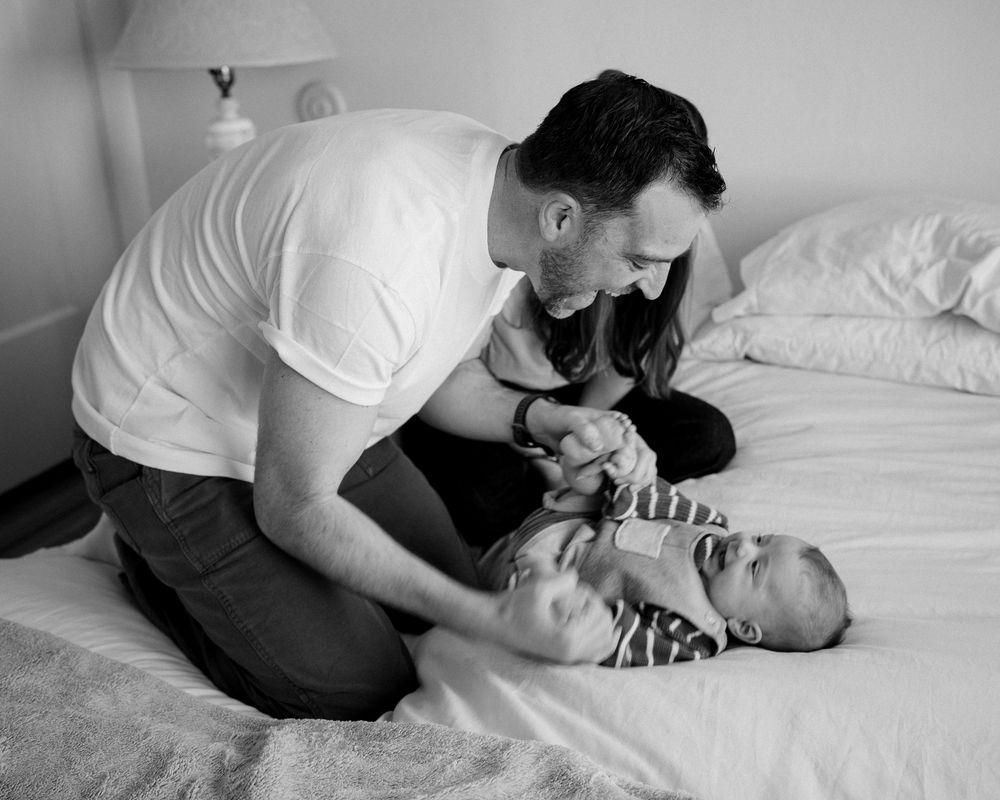 Black and white photo of a father and mother playing with their smiling baby on a bed.
