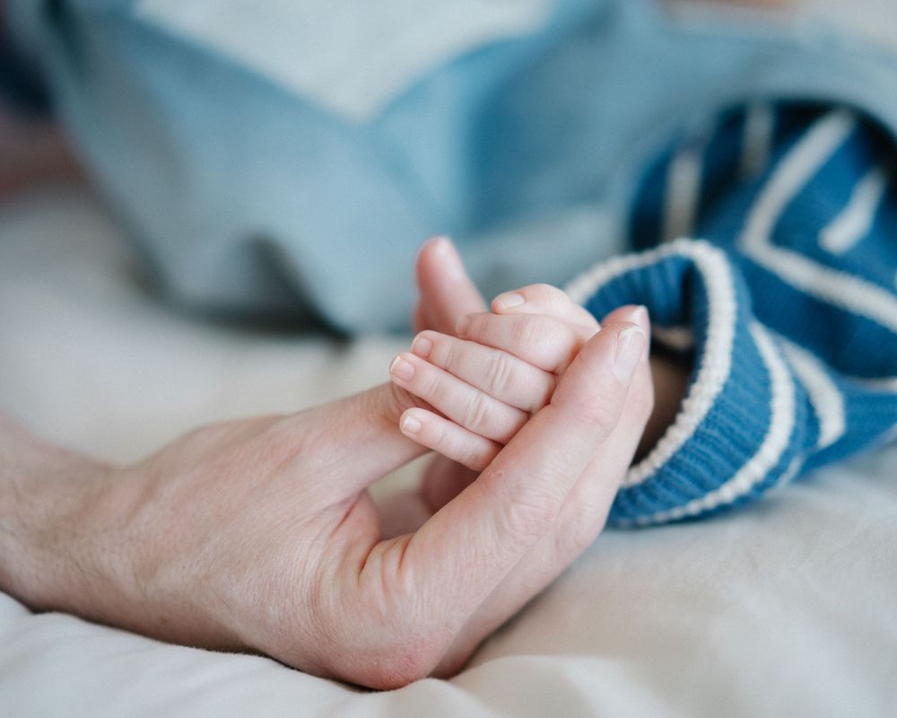 A newborn baby grasping an adult's finger, symbolizing new life, family bond, and parental love.