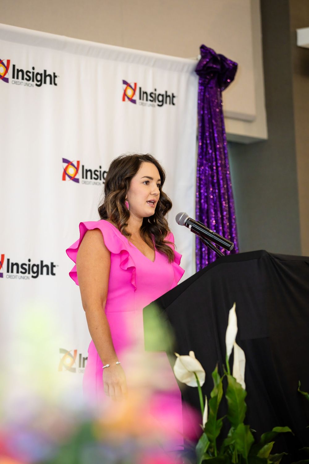 Woman in pink ruffled dress speaking at podium with Insight Credit Union branded backdrop.