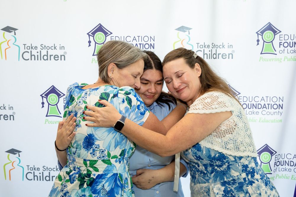 Three people share a warm group hug at a Take Stock in Children Education Foundation Take County event.