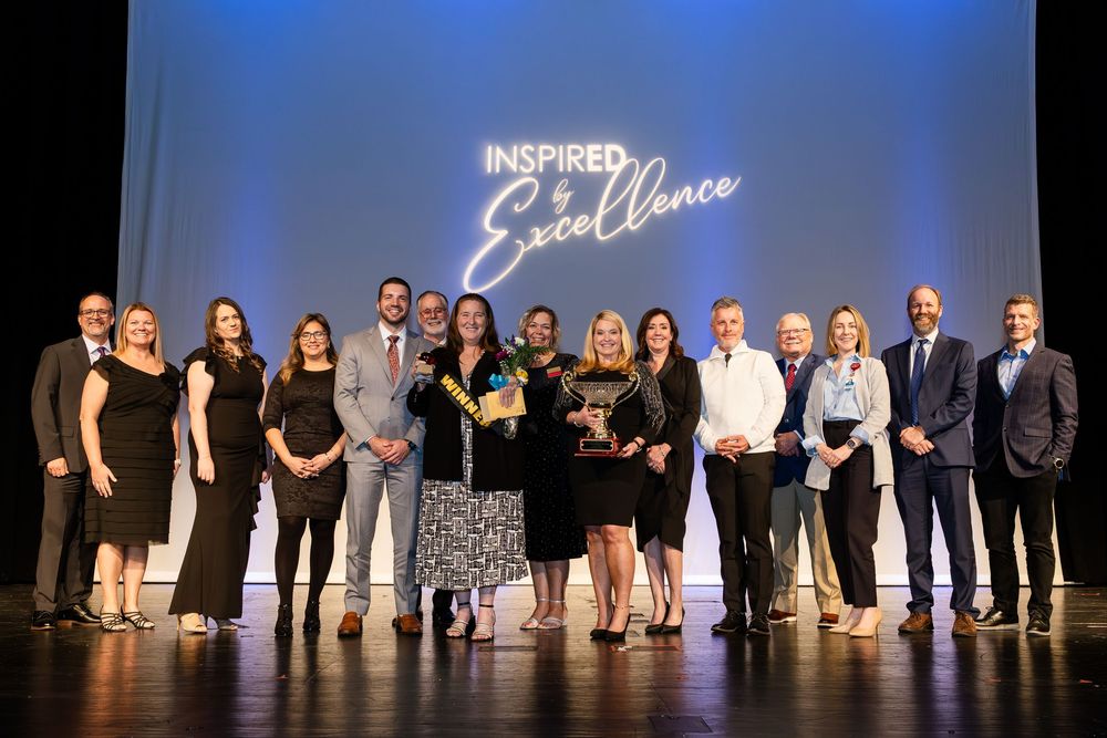 Group of professionals posing on stage at Inspired Excellence awards ceremony under neon sign.