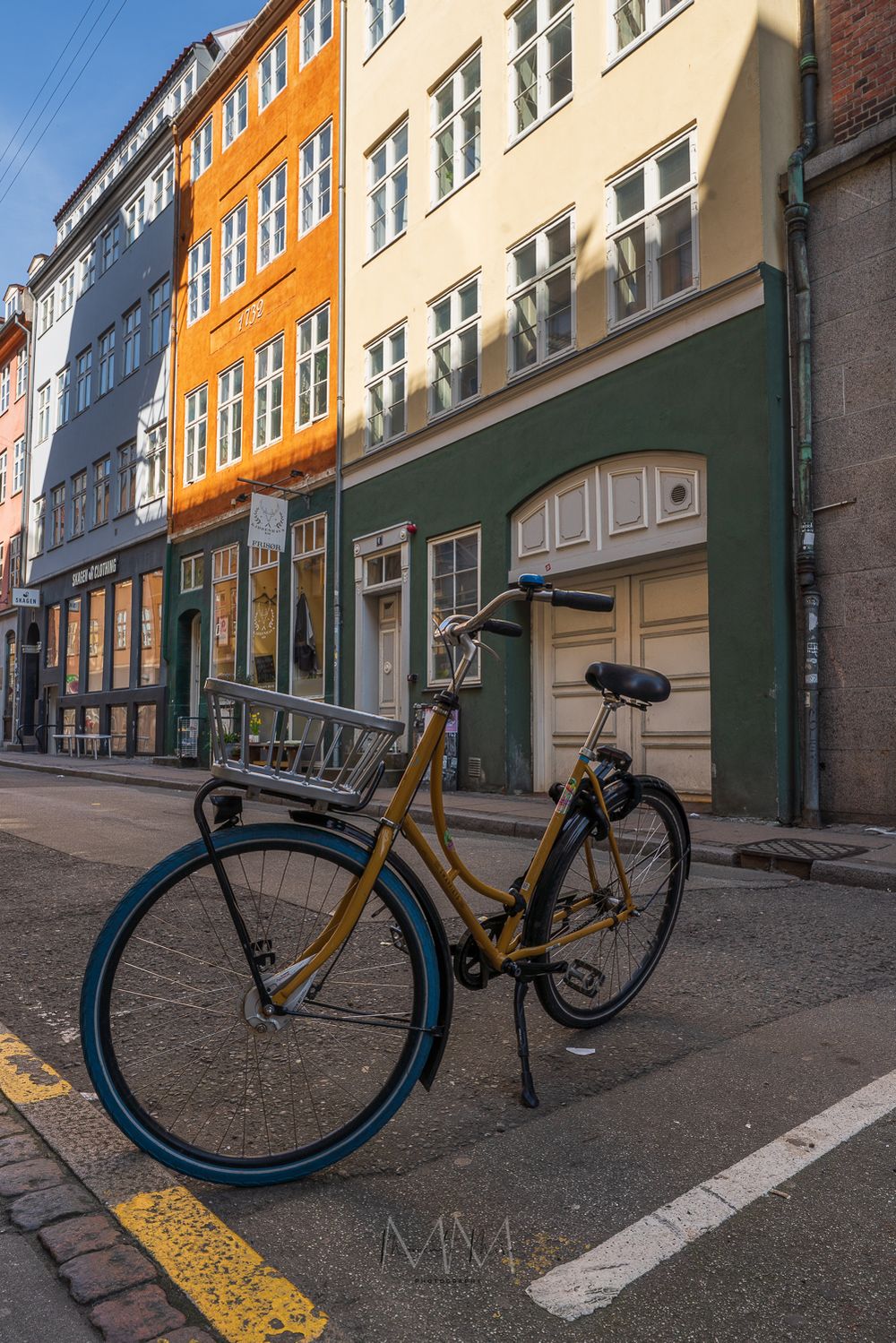 Vintage yellow bicycle parked on cobblestone street beside colorful Copenhagen buildings.