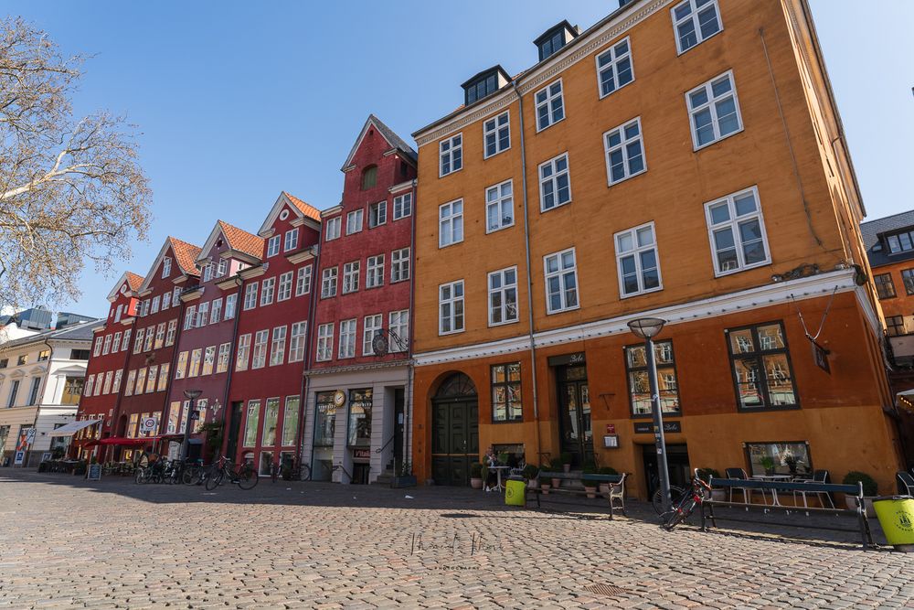 Historic colorful Danish buildings lining a sunny cobblestone square in Copenhagen.