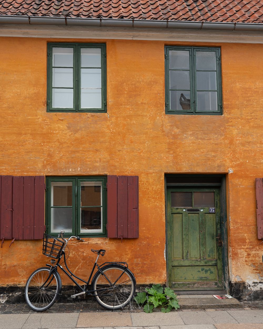 Orange Danish house facade with green shutters and black bicycle parked outside.