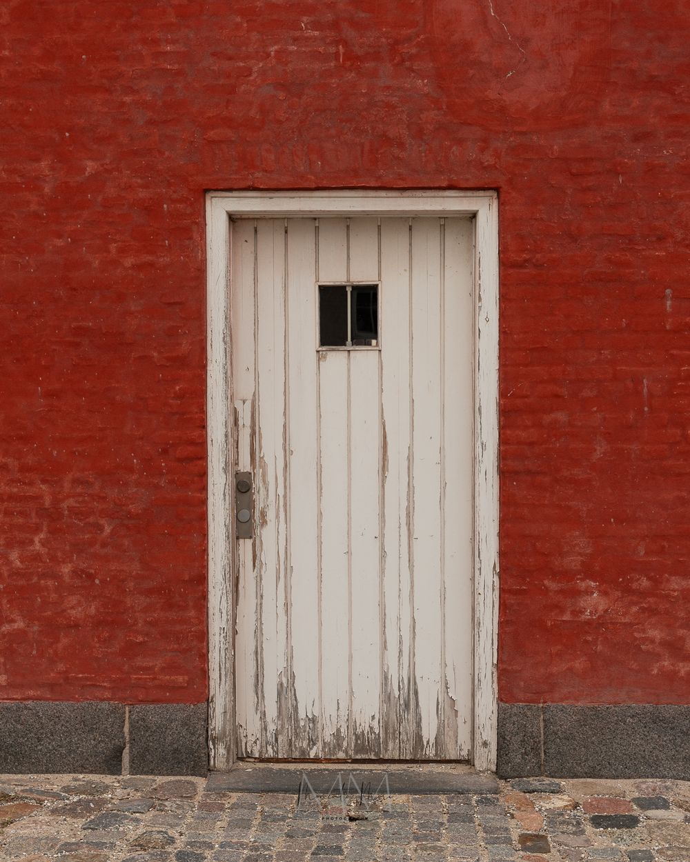 Weathered white wooden door with peeling paint set in red brick wall.