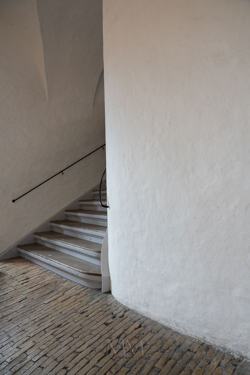 Minimalist white stucco staircase with iron handrail and ancient brick floor in historic building.