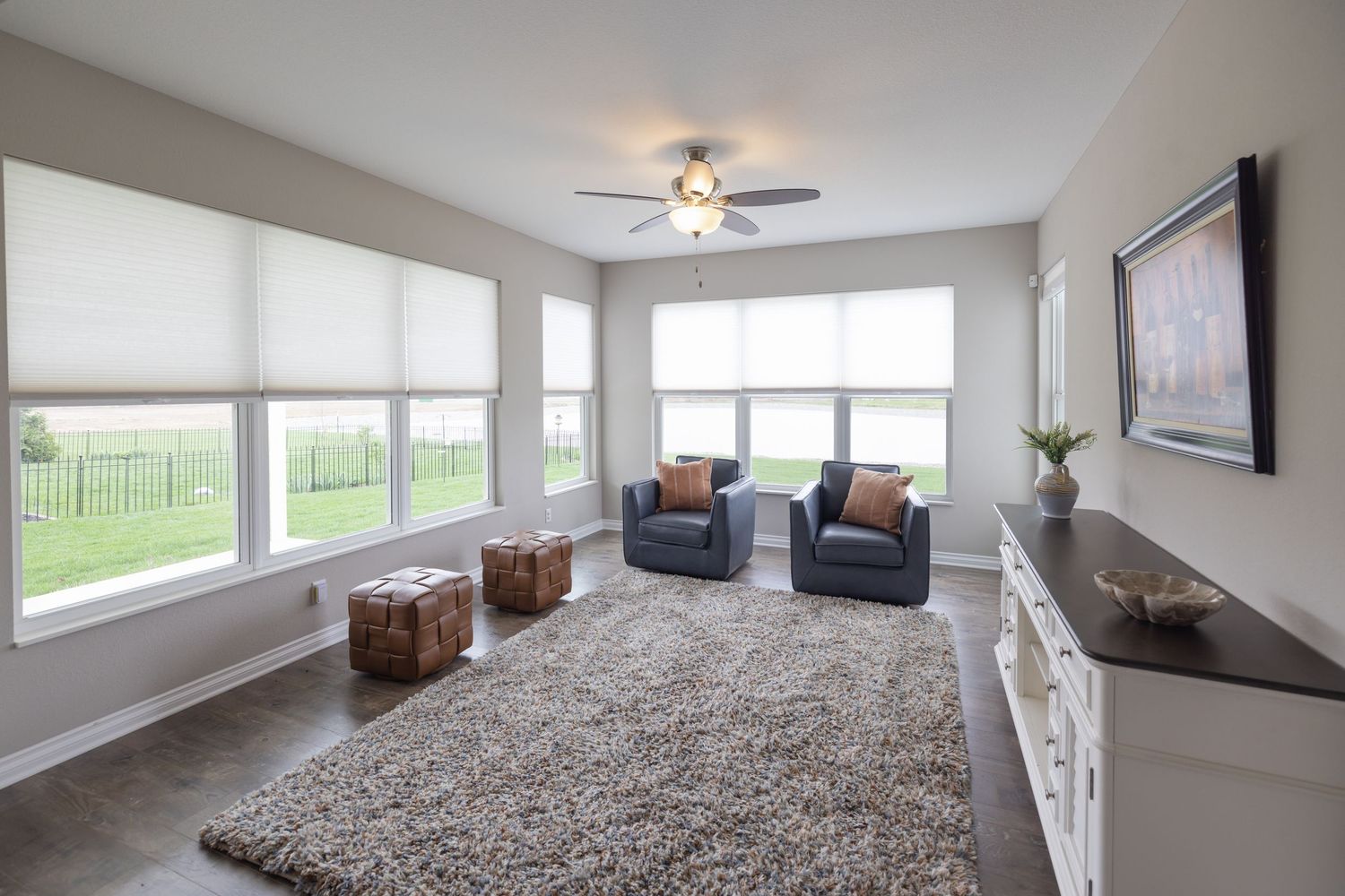 Bright living room with blue armchairs, shag rug, roller shades on large windows, ceiling fan, and white dresser.