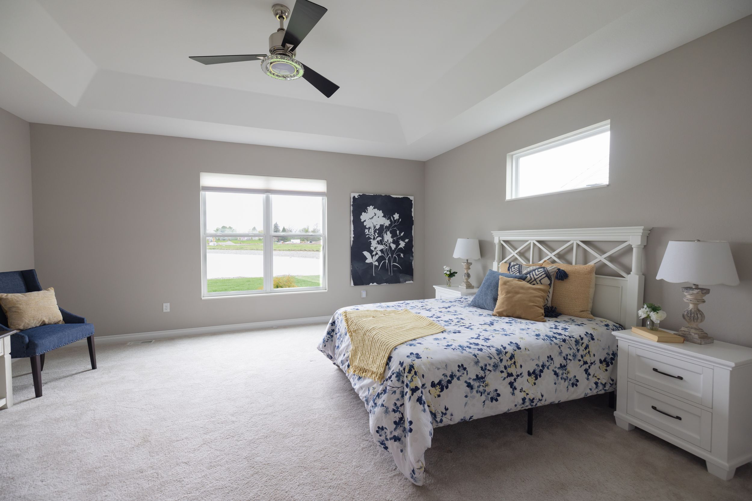 Spacious master bedroom with vaulted ceiling, ceiling fan, plush carpet, white queen bed, and large windows providing natural light.